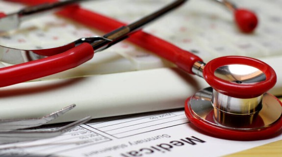 A red stethoscope resting atop a keyboard and a Medical Bill form 