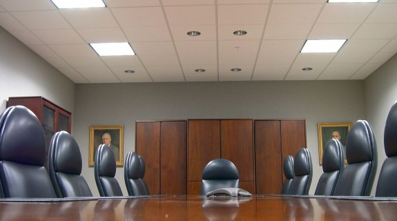 An empty boardroom with several black chairs surrounding a wooden table