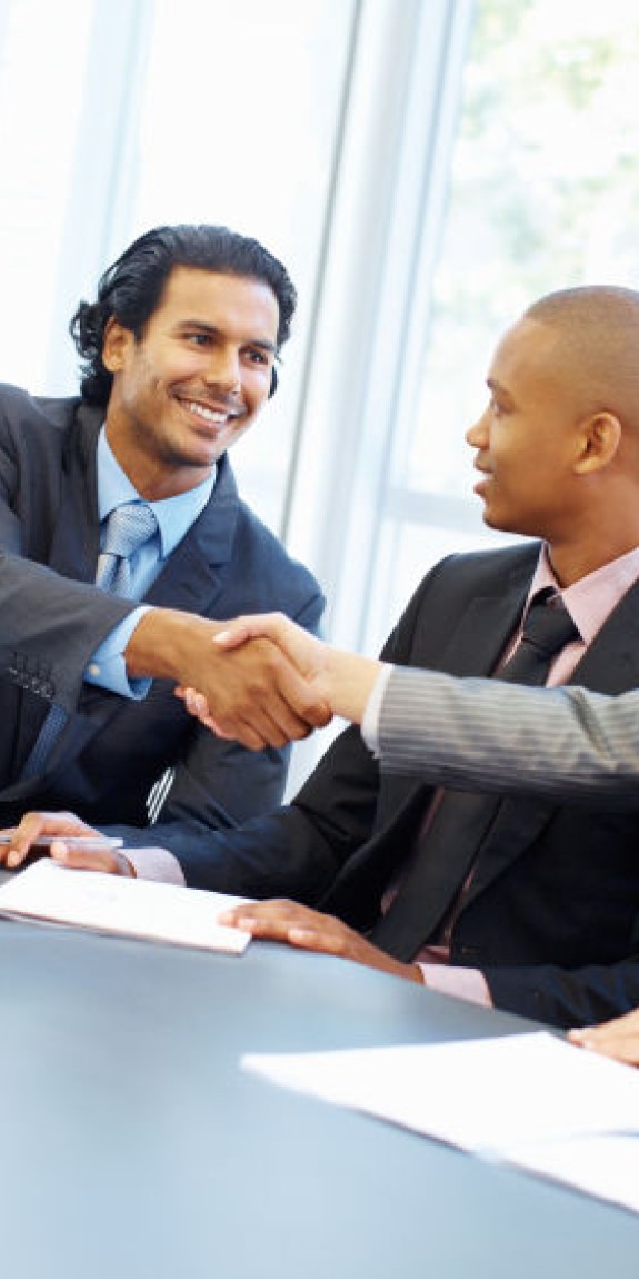 Professionals exchange a handshake across a meeting room table