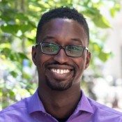 Black Man smiling in purple button up shirt.