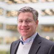 white male smiling in black jacket wearing glasses