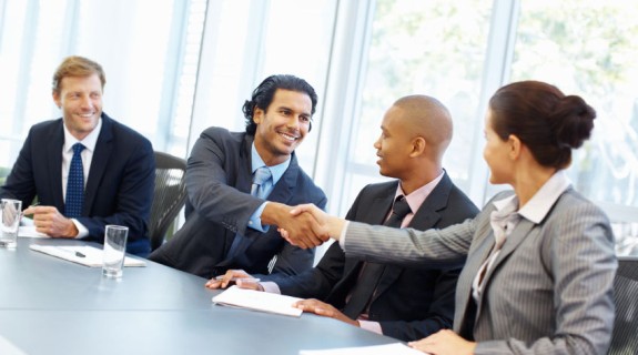 Professionals exchange a handshake across a meeting room table