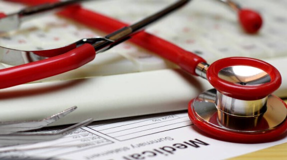 A red stethoscope resting atop a keyboard and a Medical Bill form