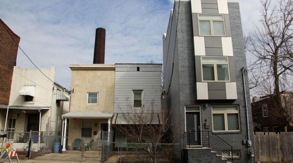 A large gray three story house next to three small two story houses.