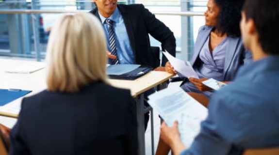 Four people in business suits sitting around a table holding papers in their hands