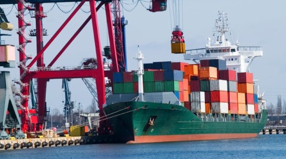 A large ship loaded with shipping containers docked at a harbor