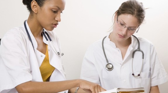 Two female healthcare professionals looking at an open book