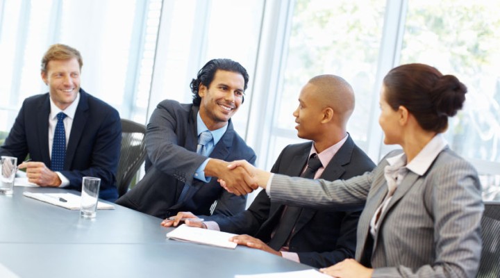 Professionals exchange a handshake across a meeting room table
